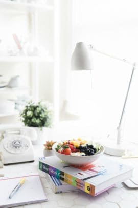 A fruit salad in a bowl on top of a colorful cookbook on a desk.